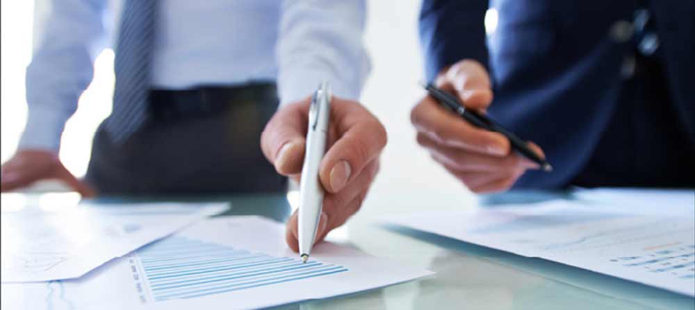 Two people with a pen pointing at a sheet of paper