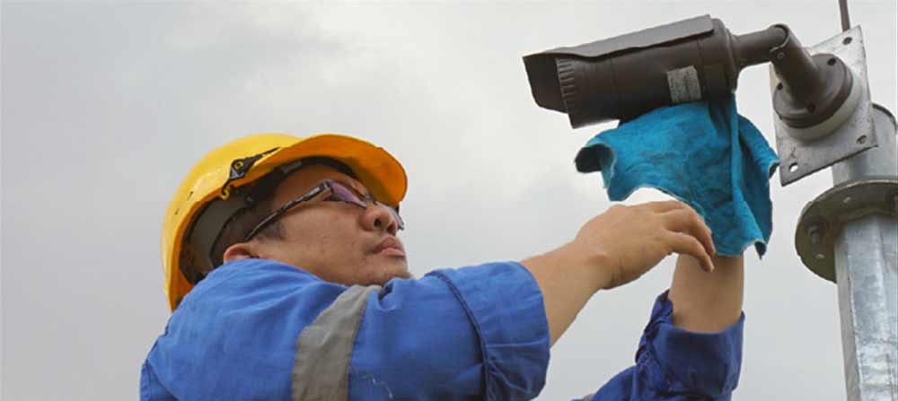 Man in hard hat installing a camera to the side of a building