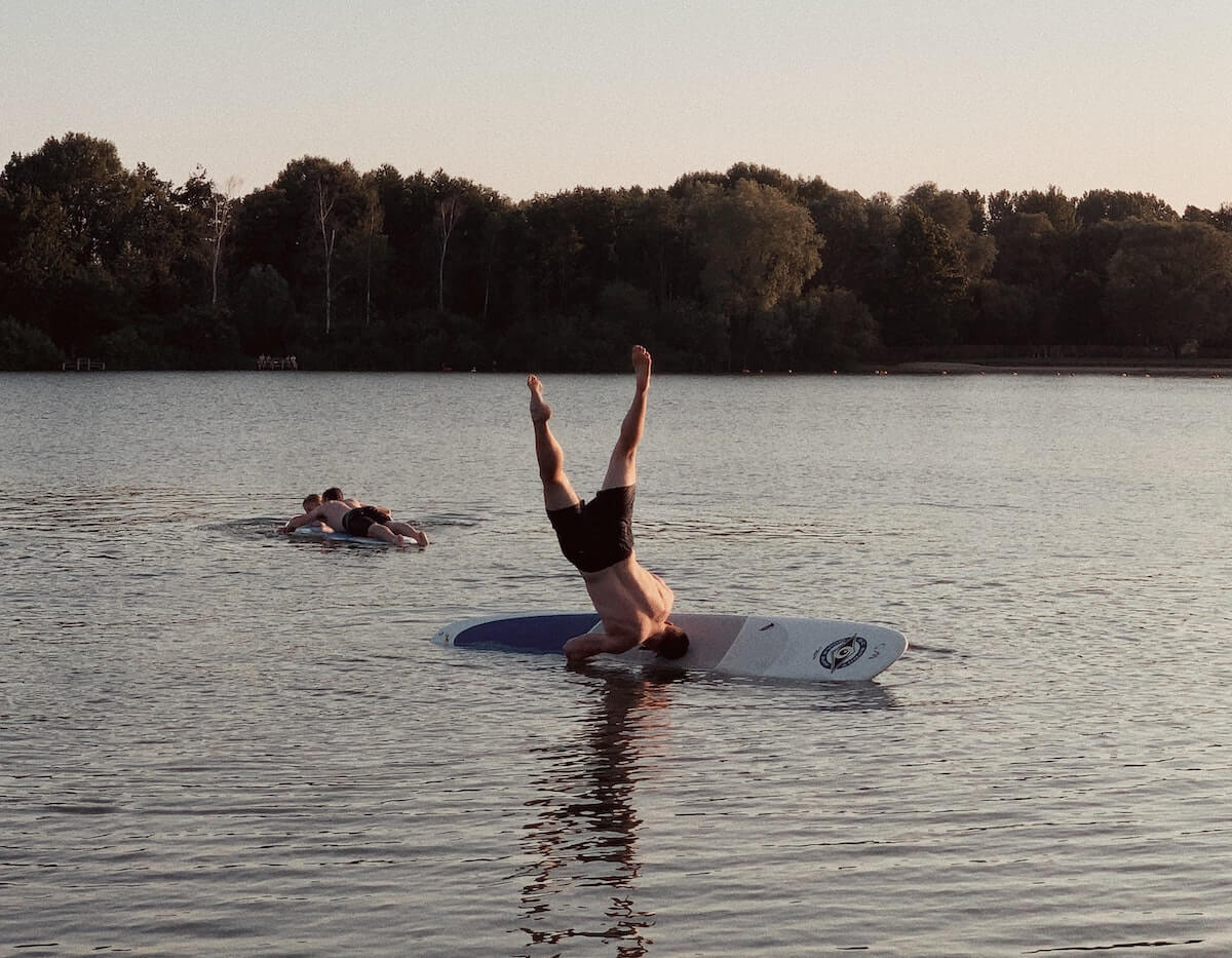 En man står på händer på en surfbräda och ramlar av