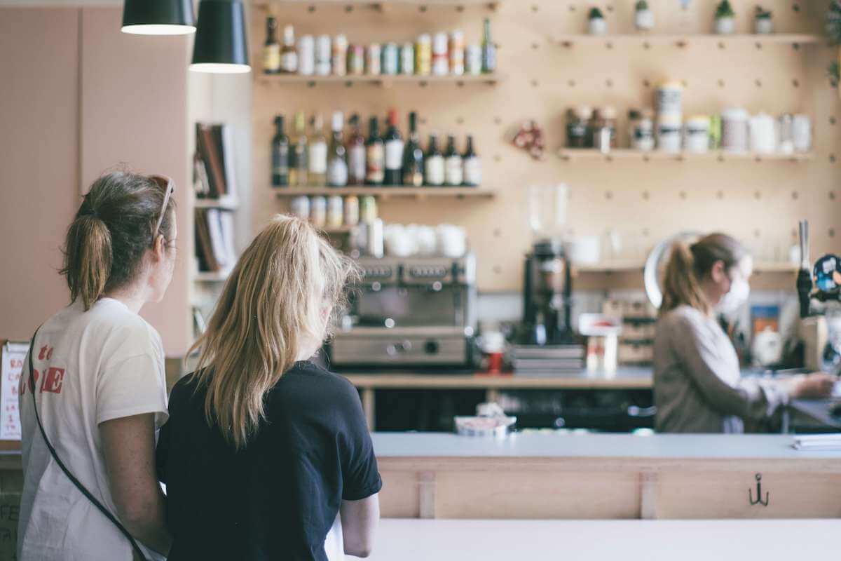 Två tjejer väntar på servering vid en bardisk av en kvinna med munskydd under pandemin