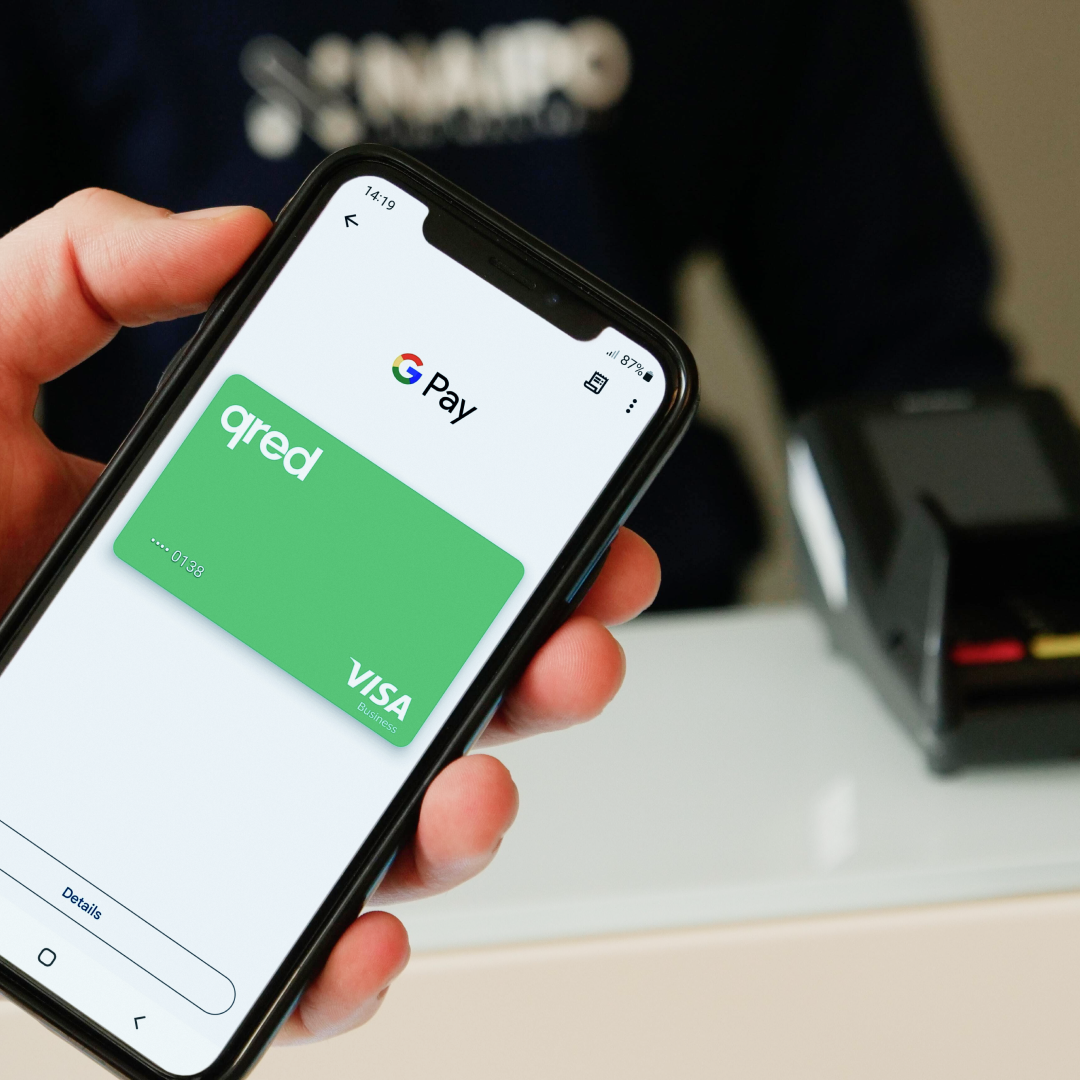 Hand med mobil som kommer att använda Qred VISA med Google Pay på en fysisk kortterminal