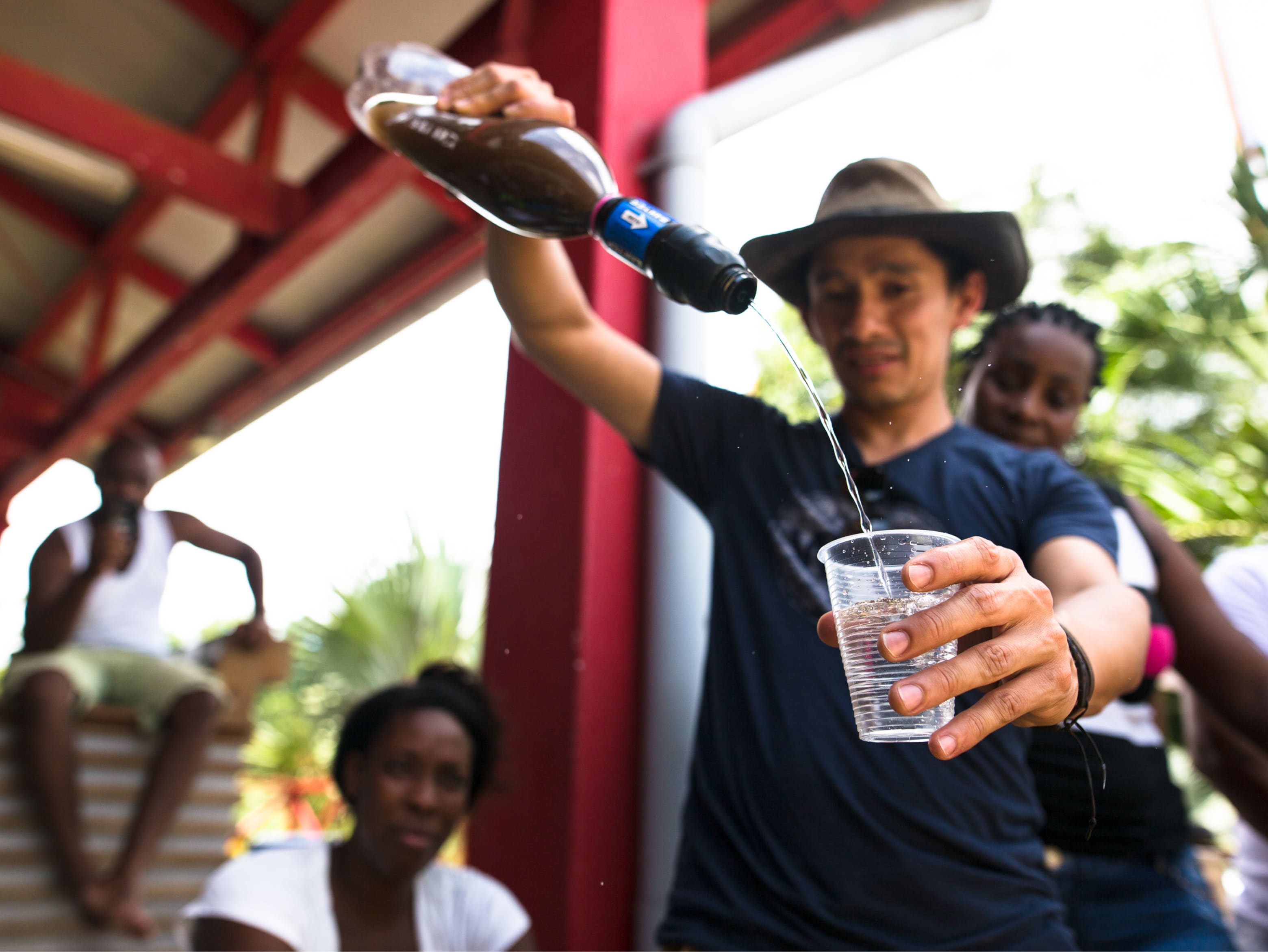 A Sawyer volunteer pours water from a Sawyer filter into a cup. The water in the filter is murky and what comes out is clear.