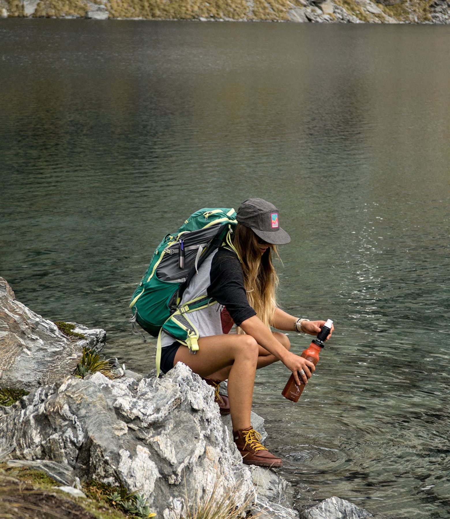 A woman fills her Sawyer filter from a river.