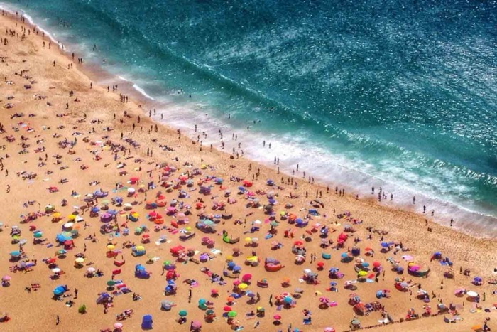 Photo of beach filled with people and umbrellas next to ocean