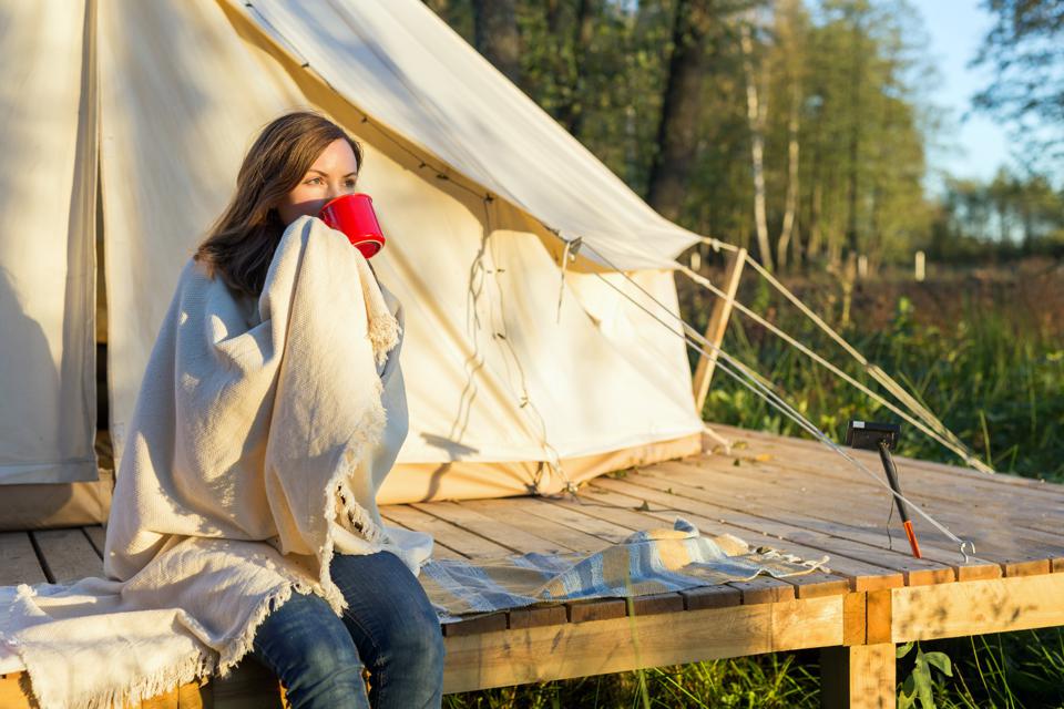 Woman drinks from cup in front of tent