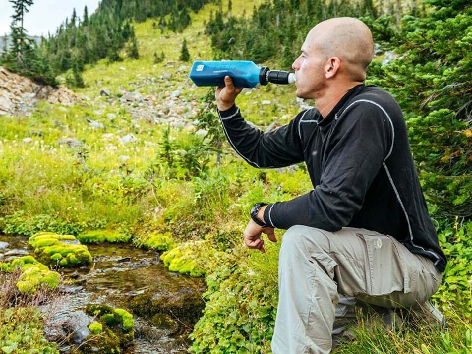 Man drinks from sawyer filter next to stream