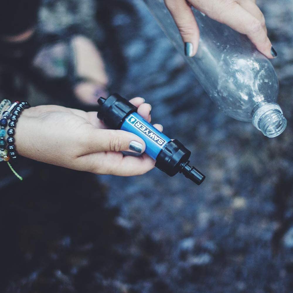 Hand holding Sawyer water filter and plastic bottle