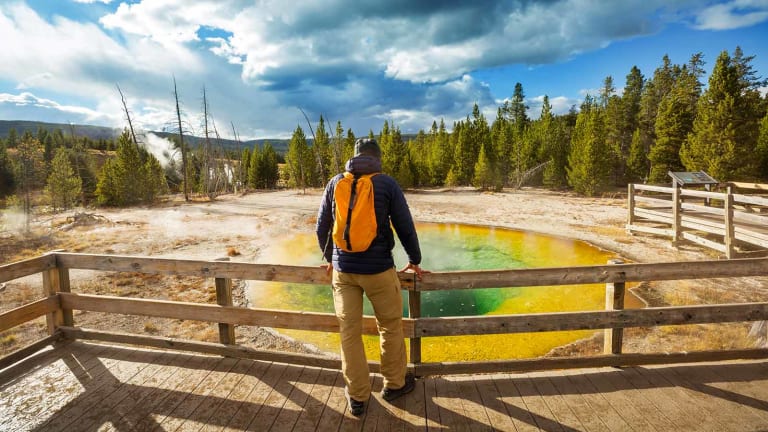 Hiker on wooden deck looking at geyser