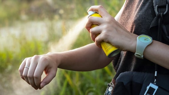 Person spraying mosquito repellent on arm