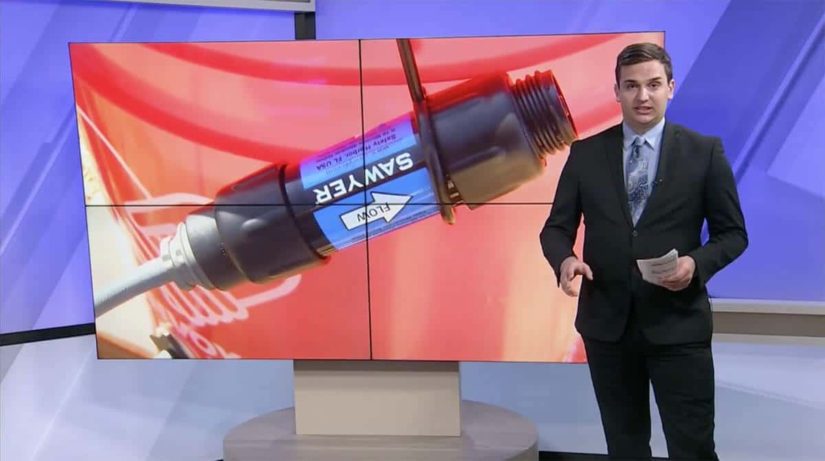 Screen capture of news anchor in front of Sawyer filter on screen behind