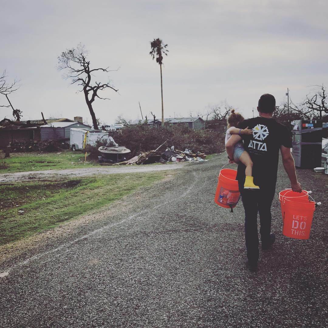 Man carrying child and Sawyer bucket water filters to destroyed community