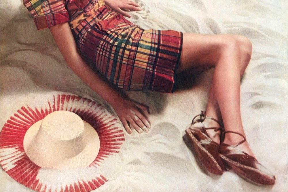 Person sits in sand next to hat with summer shoes