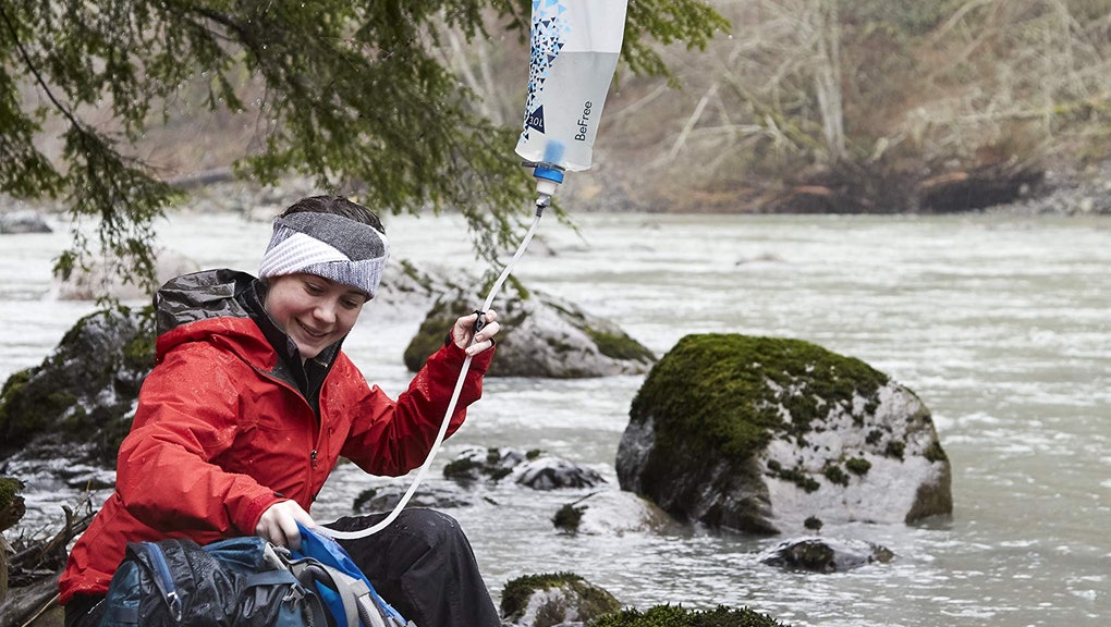 Backpacker using gravity water filter next to river