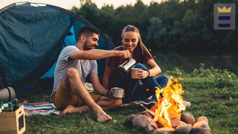 Couple sharing coffee next to fire in front of tent