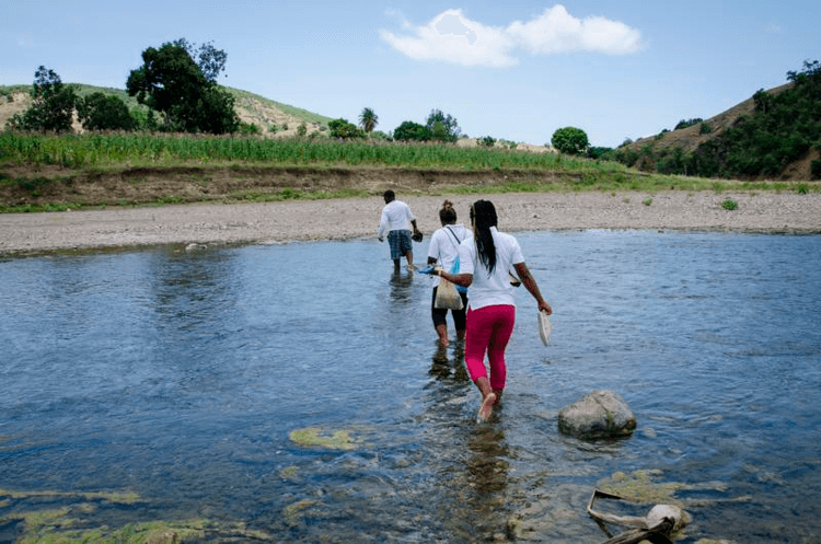 Three Haiti people cross stream barefoot