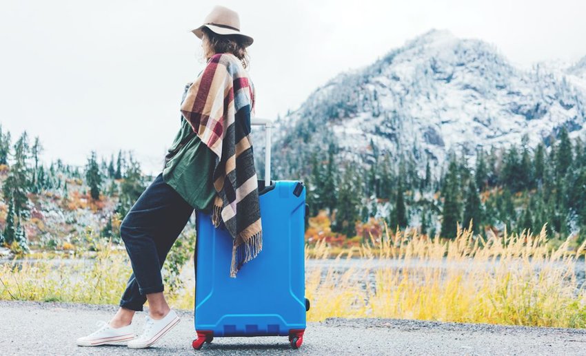 woman leaning on suitcase in front of mountain