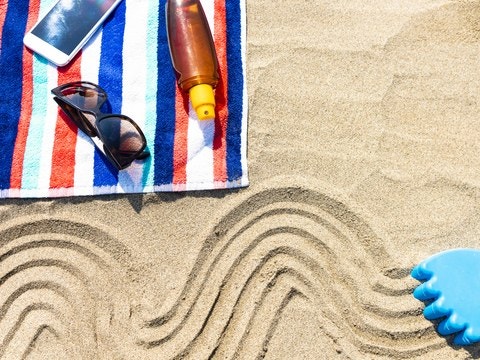 A towel on sand with sunglasses, sunscreen and a phone