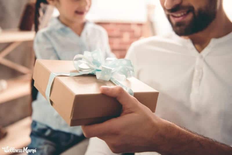 Dad holds gift with bow in hand next to child