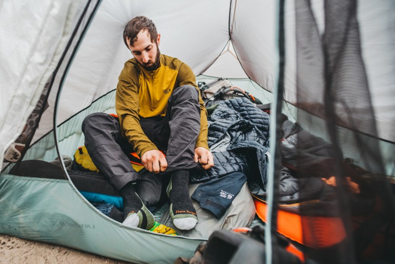 Man putting on Darn tough socks in tent