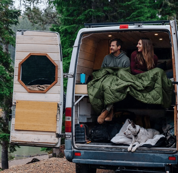 Couple sits looking out back of camper van