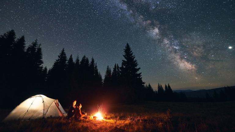 Campers next to tent by fire under stars