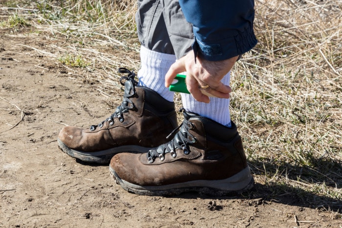 Person wearing hiking shoes spraying tick repellent on shoes