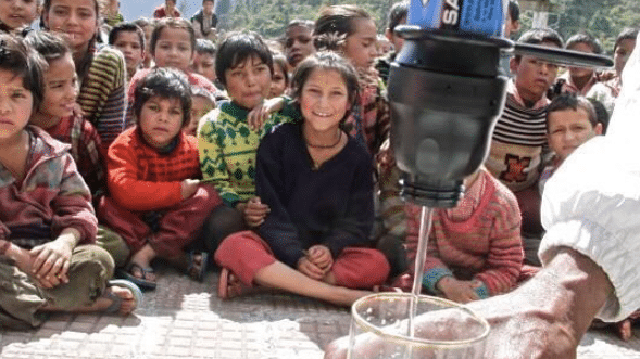 Village children sit and watch person filter water from Sawyer filter into a drinking glass