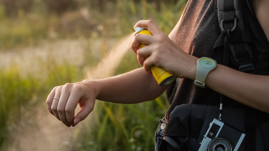 Person sprays insect repellent on arms