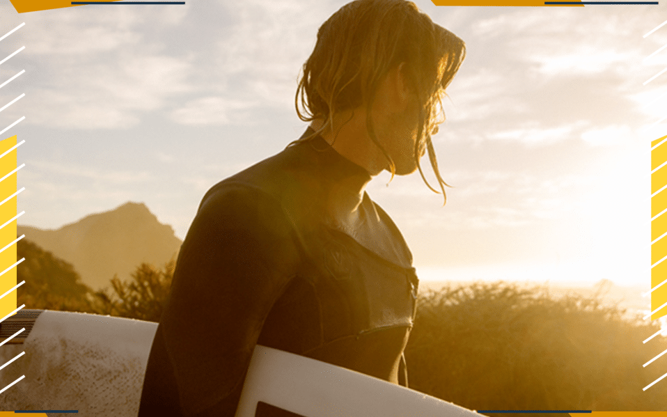 A surfer holds surf board looking off into sunlight