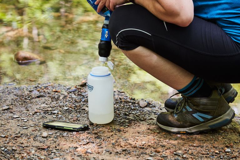 Person filtering water from Sawyer filter into water bottle