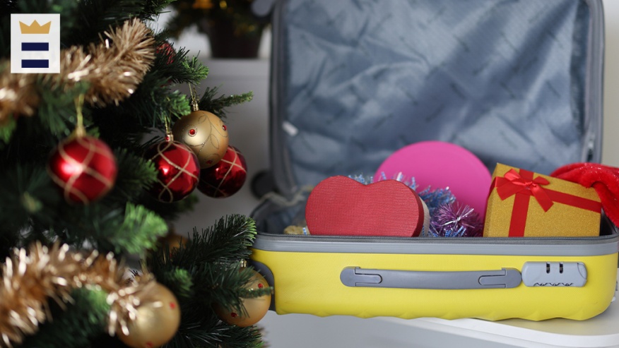 A Christmas tree on left with a suitcase of presents on the right