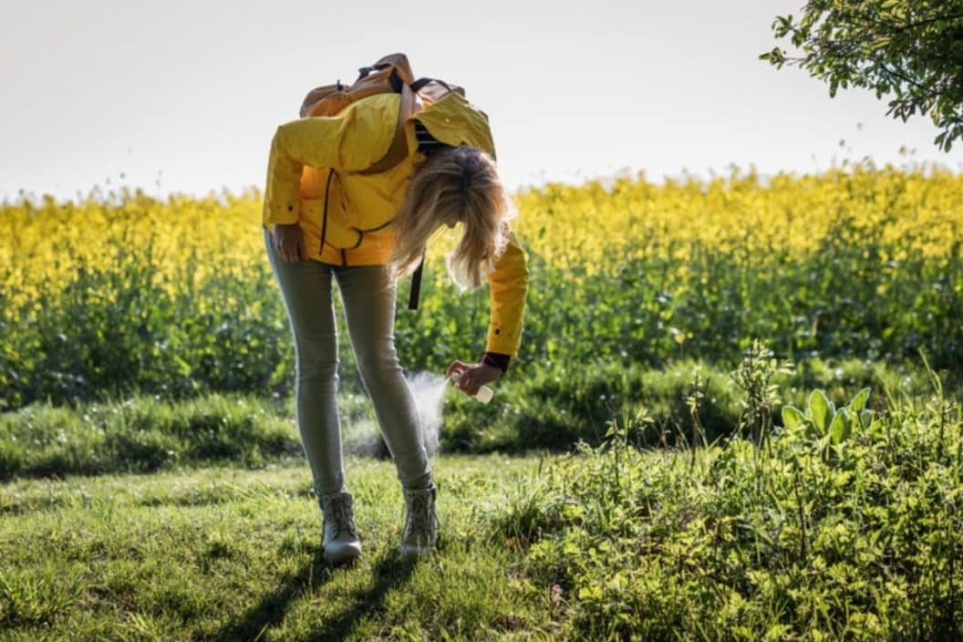 An individual spraying insect repellent on their legs in a field. 