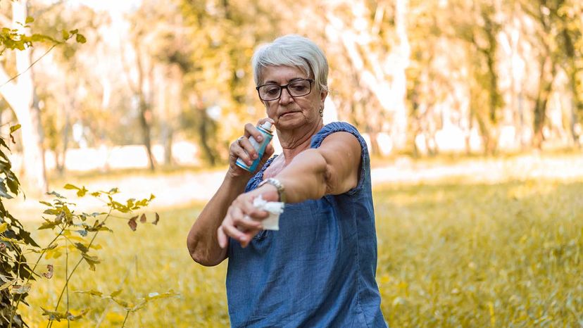 Mujer mayor rociándose repelente de insectos en el brazo. 