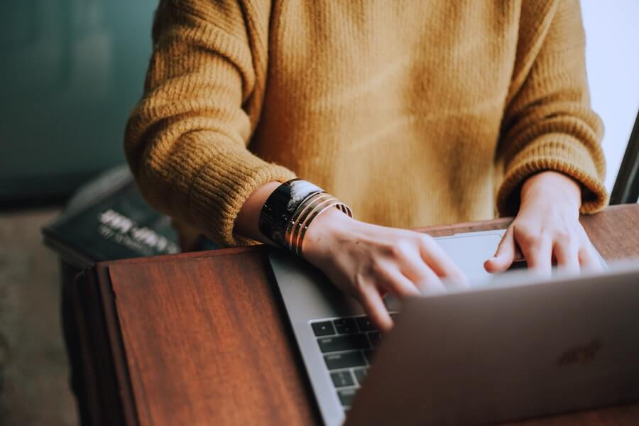 woman typing on laptop with book on her lap online nursing student advanced practice nursing school