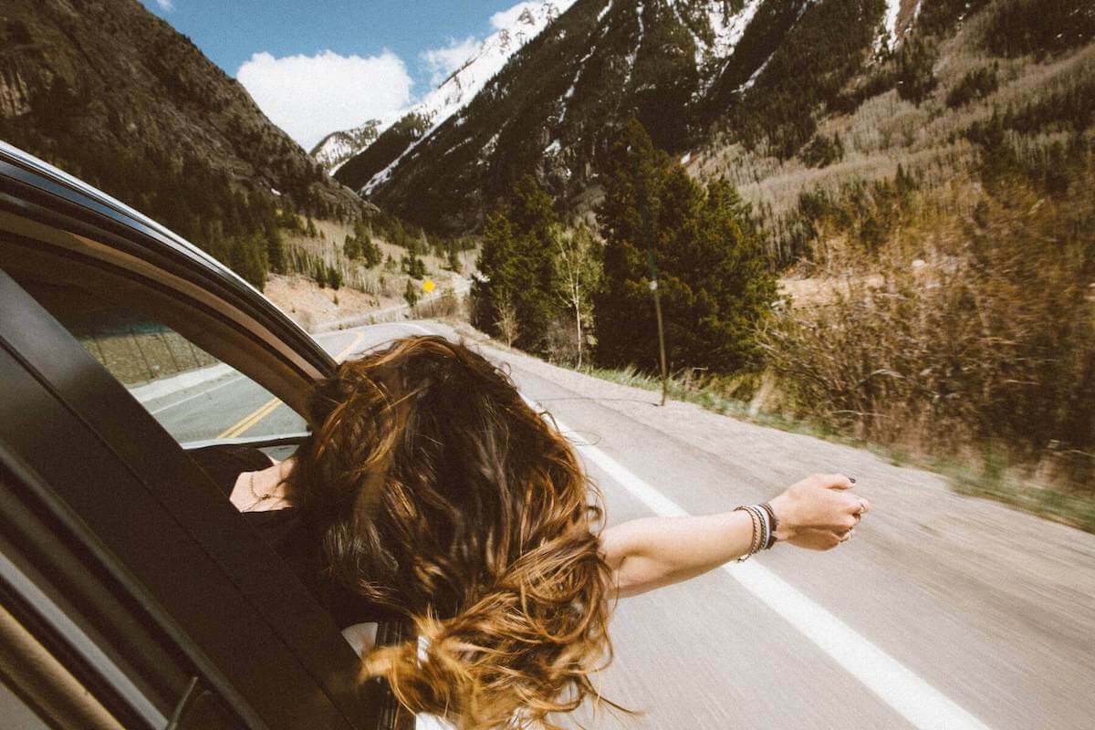 woman leaning out of car window driving up toward mountains travel nursing agencies choosing a travel nursing assignment