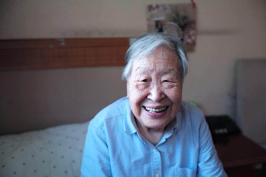 elderly woman sitting on bed and smiling into camera