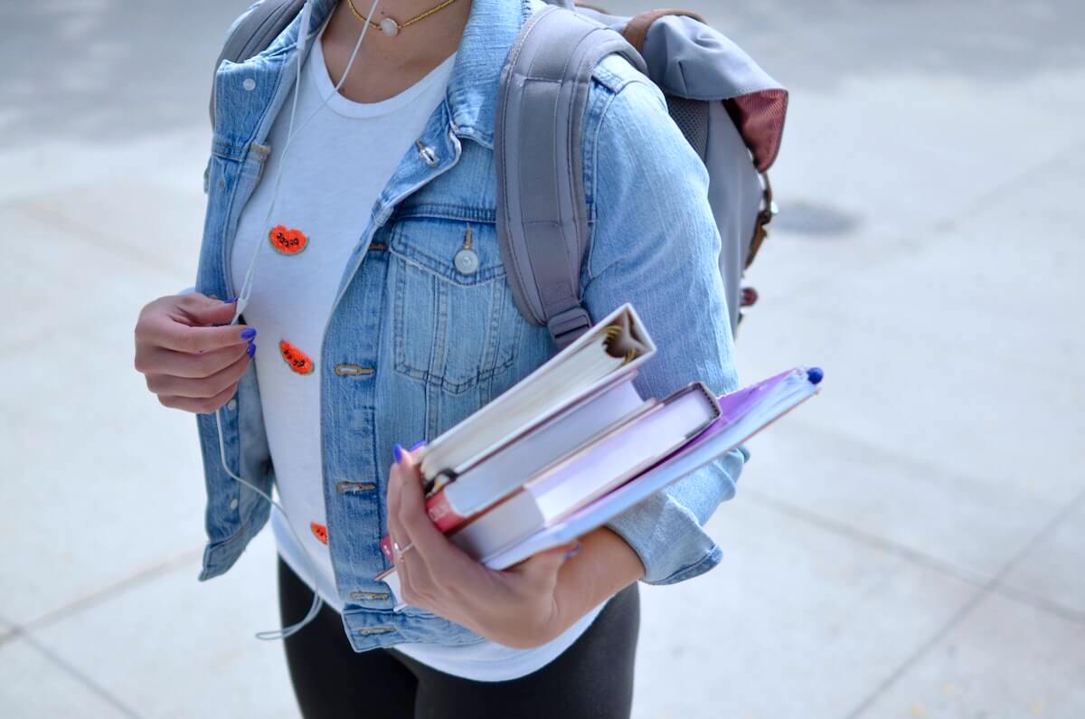 female student carrying books listening to headphones paying of nursing school debt