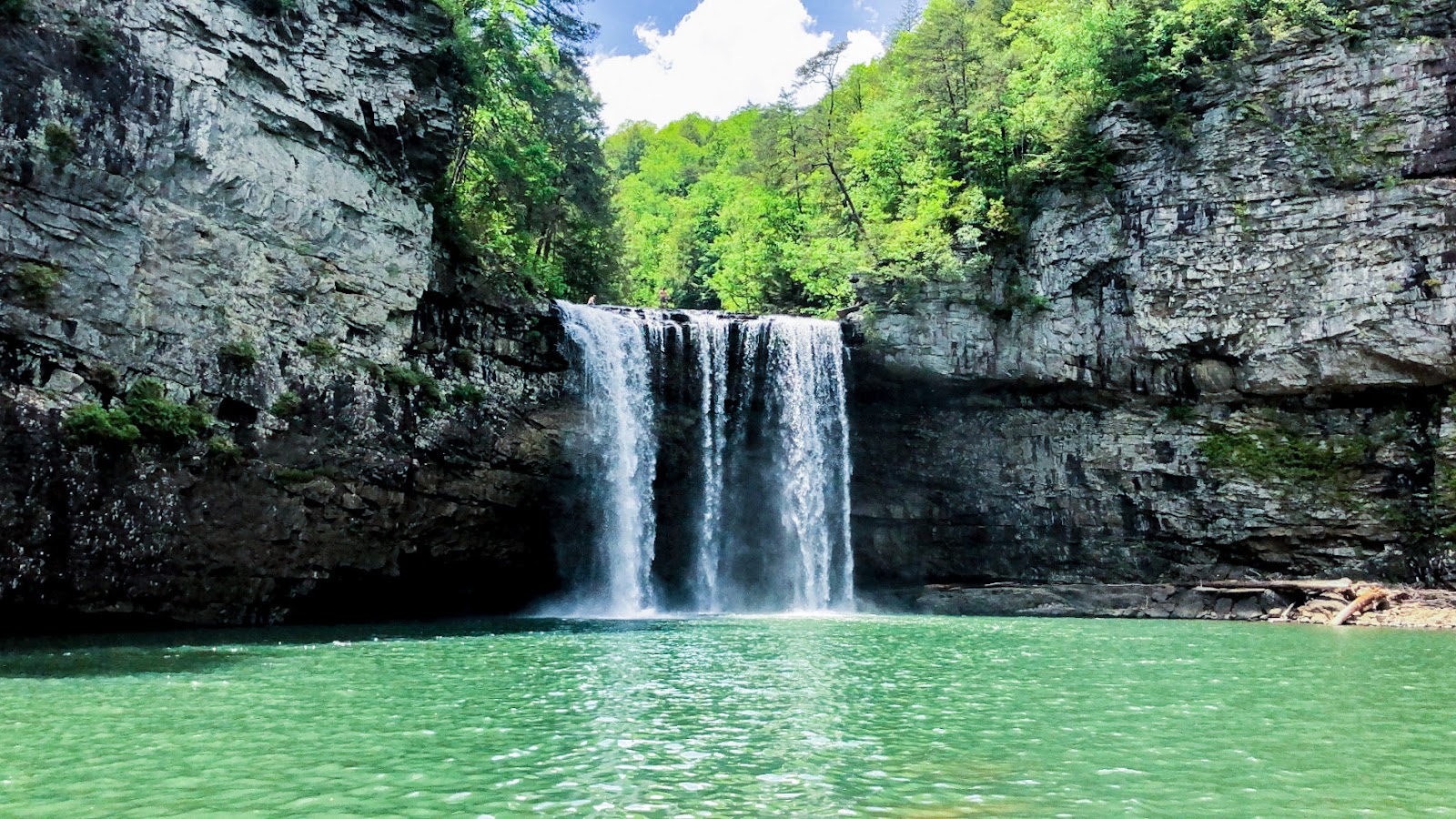 Image of a waterfall over a pretty green lake.