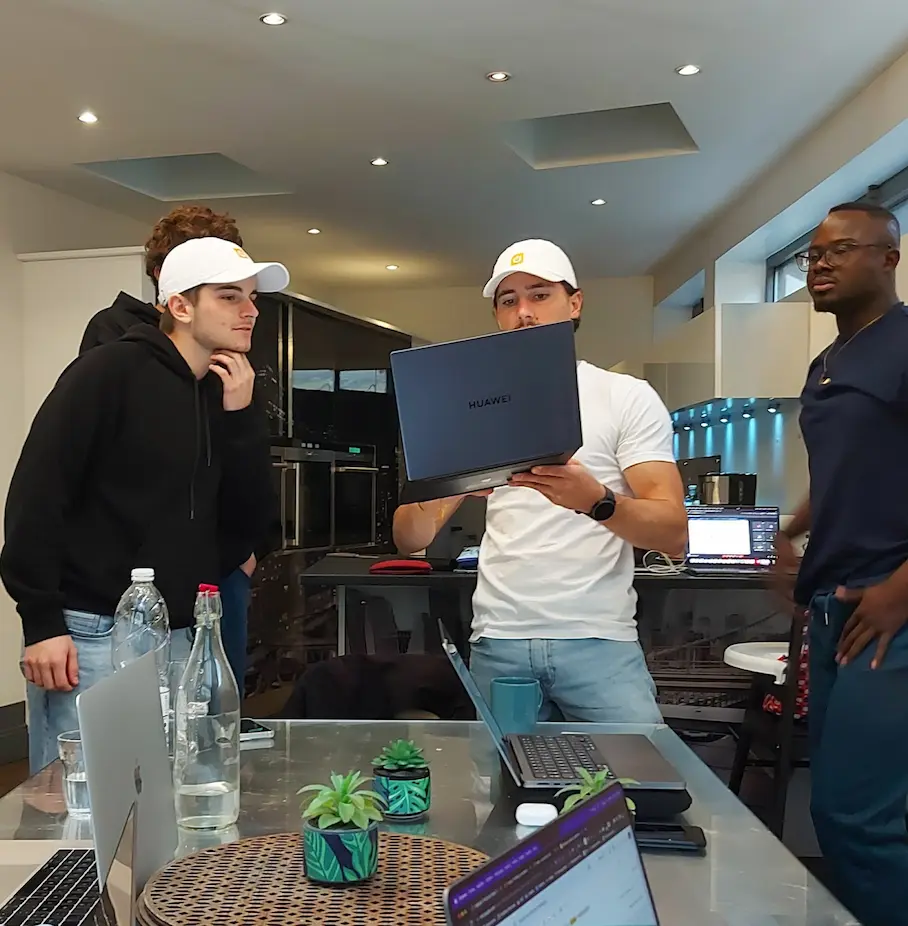 Thomas habillé avec le t-shirt et la casquette Digidop, tenant un ordinateur pour présenter quelque chose à Mérieux et Quentin de l'équipe