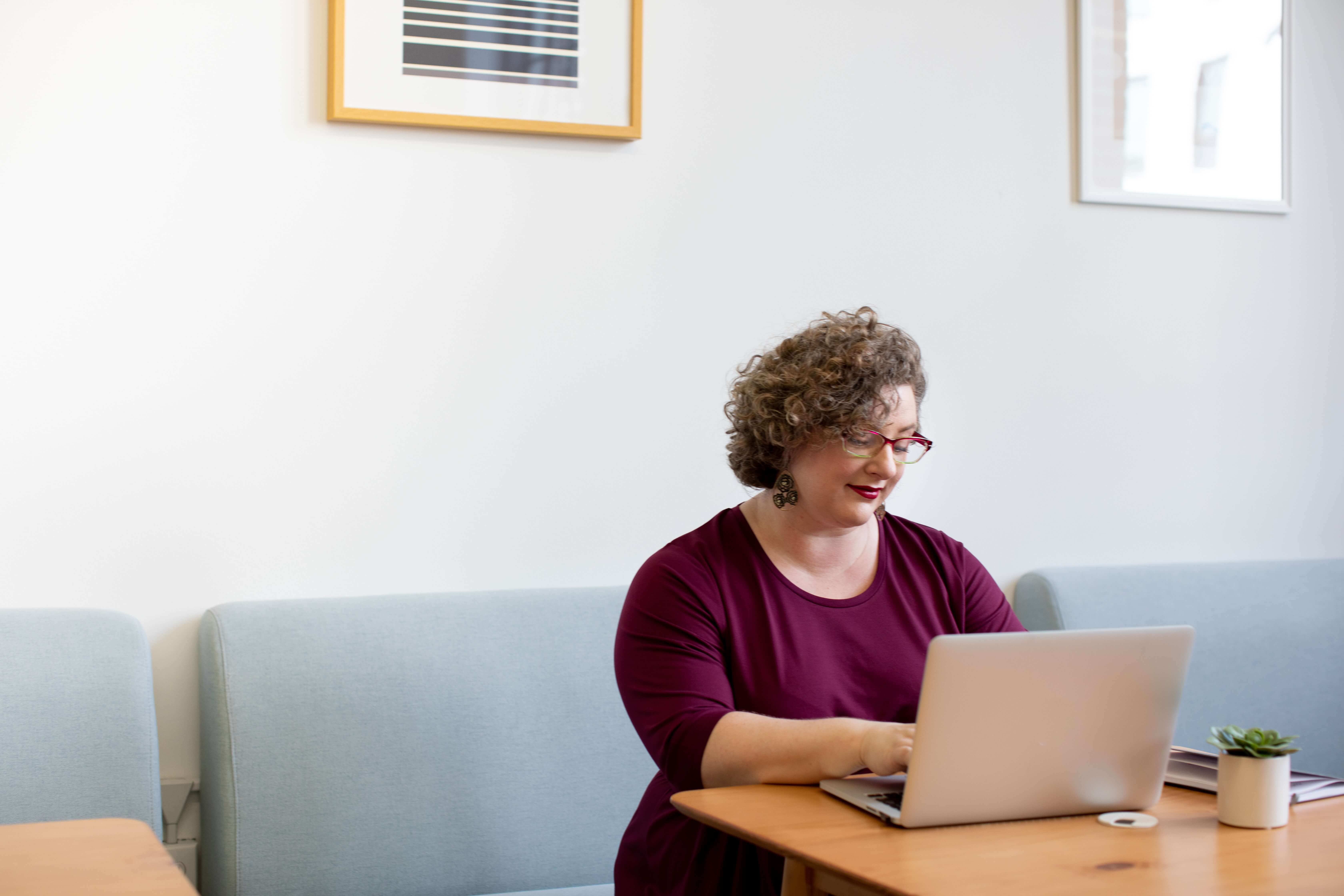 a woman wearing a purple shirt works on a laptop