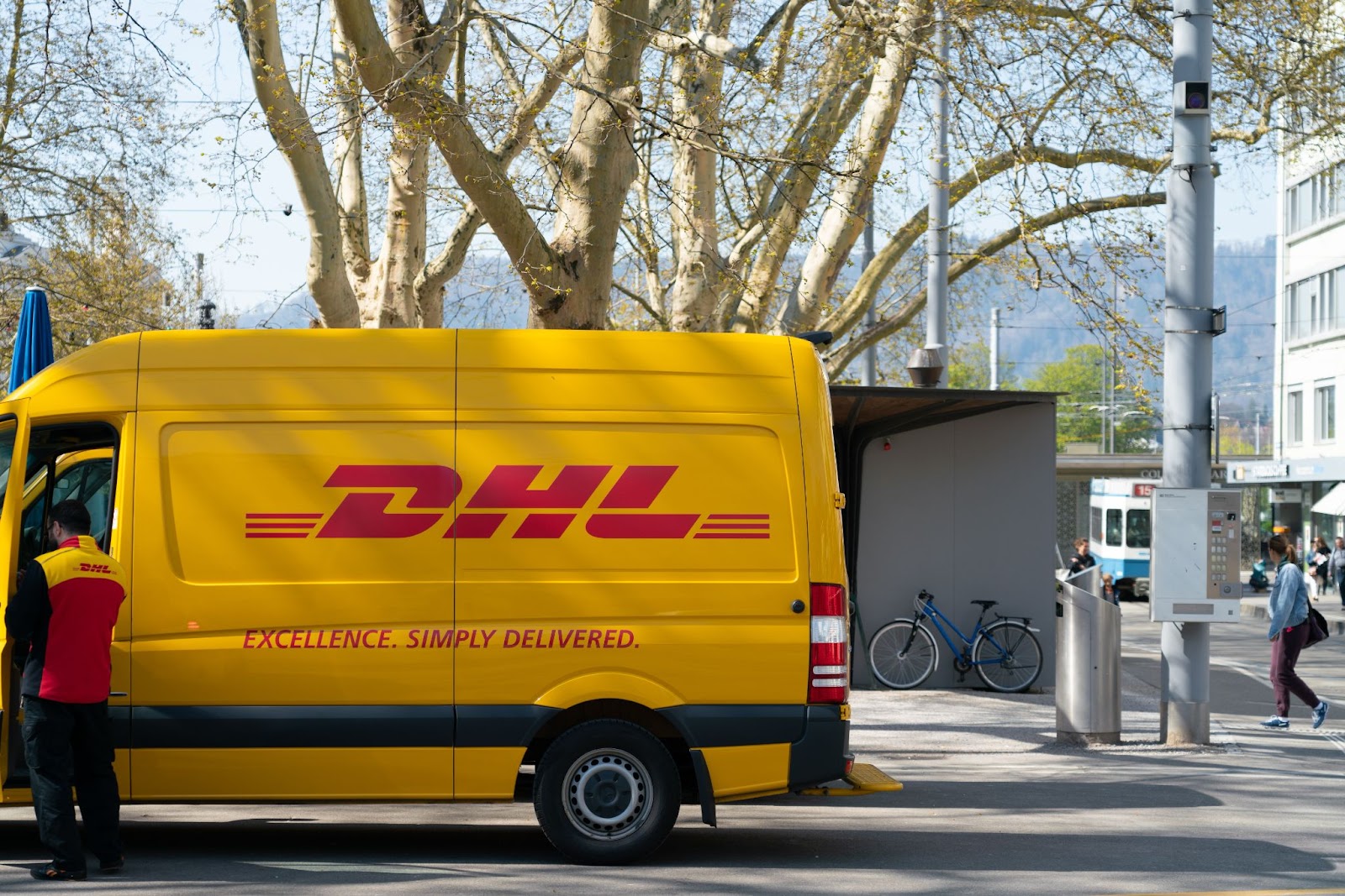 image of a DHL postal van and delivery service person in the city