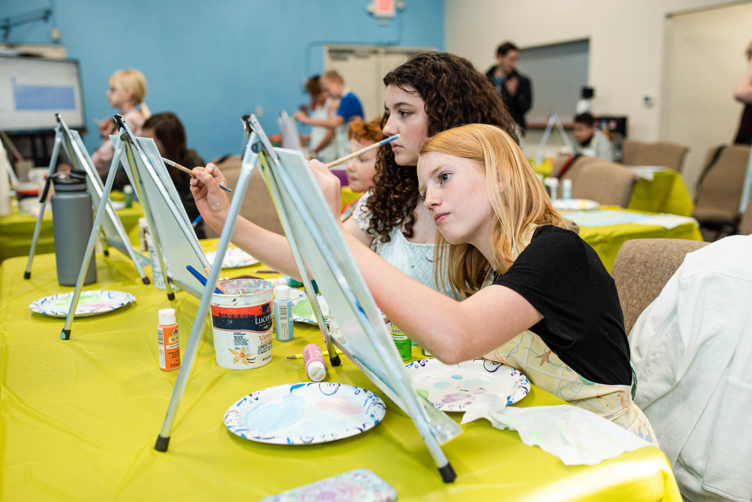 Two students painting on easels in their microschool that is in a large Christian church.