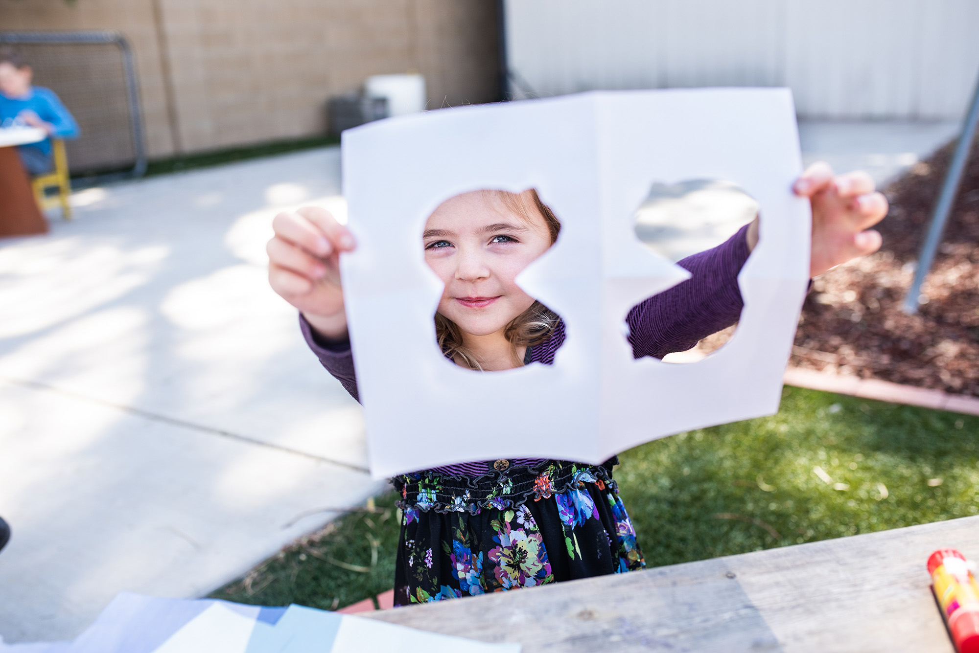 little girl looking through a cut piece of paper outside in her microschool