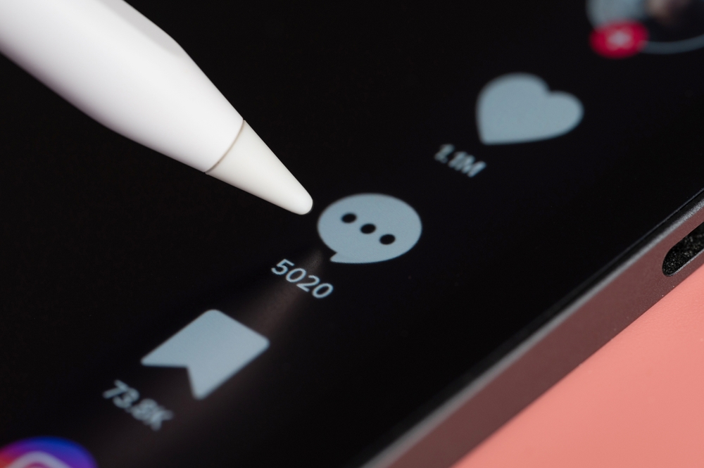 Closeup of TikTok engagement buttons and a stilus about to click the comments button.