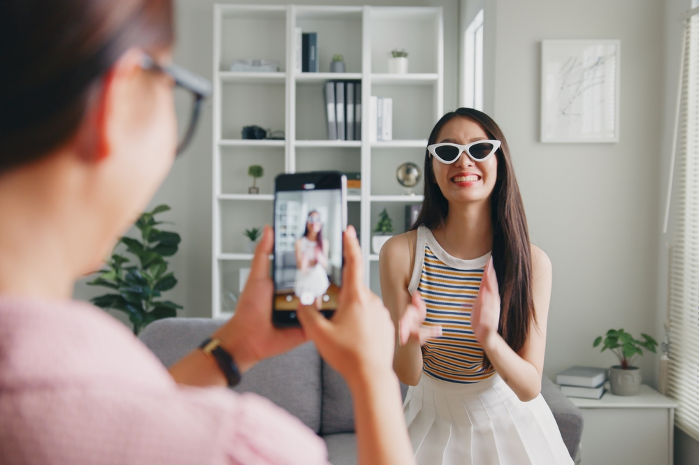 Asian woman dancing in front of the camera while her friend records her on her phone.