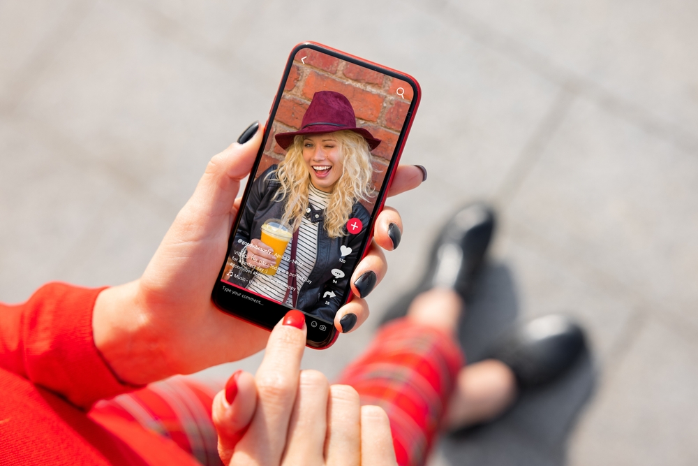 Closeup of a phone in a woman's hand that is open to a TikTok video of a blonde woman winking.