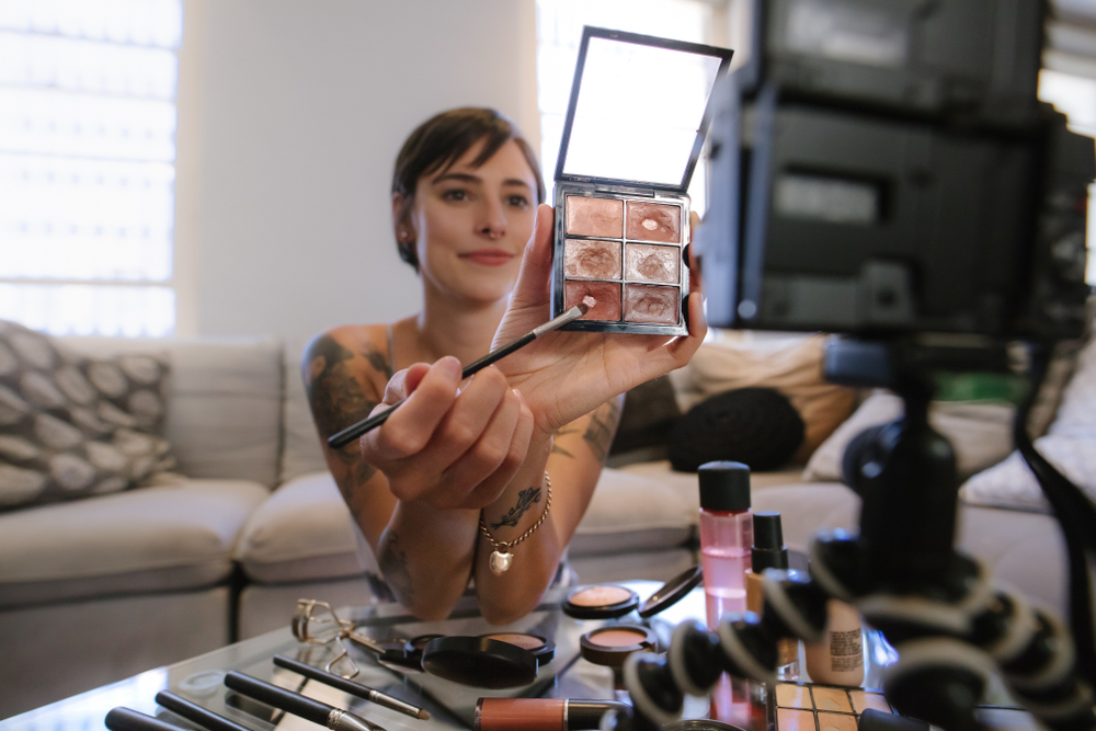 Influencer holding a makeup palette and brush up to the camera while filming a video.