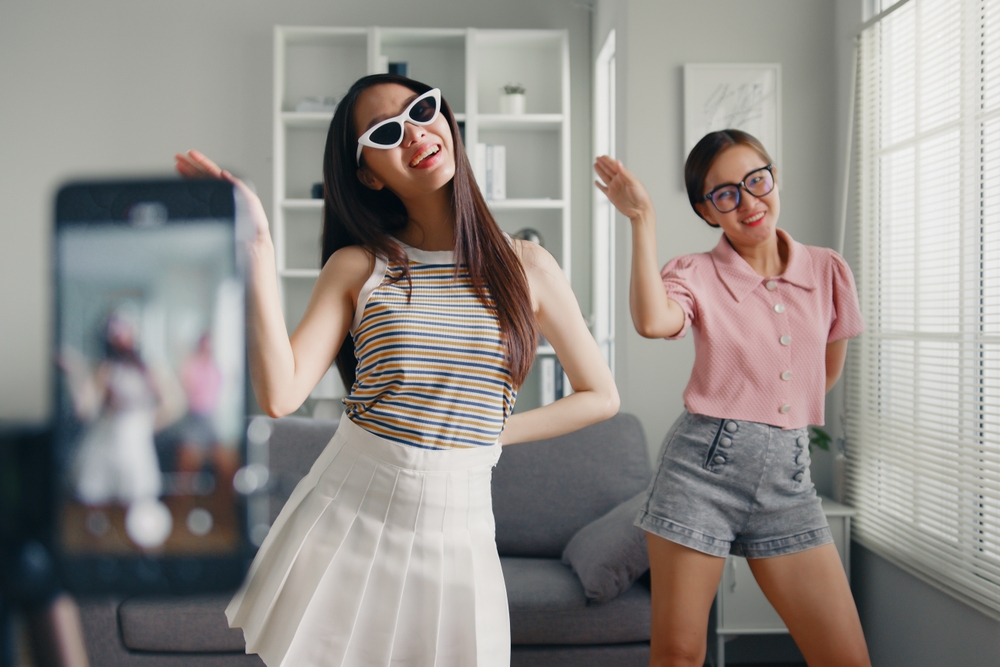 Two young asian women doing a choreographed dance while a phone records them on a tripod. 