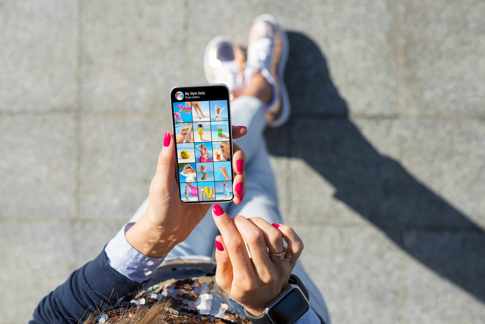 Woman walking and looking at Instagram feed with bright featured photos.