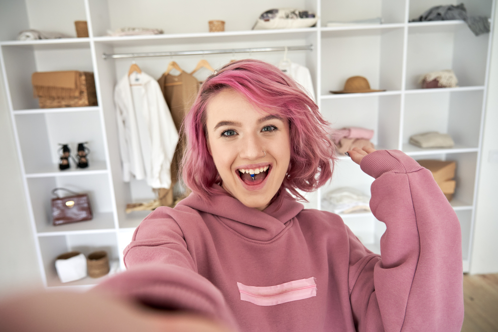 Gen Z girl with pink hair taking a selfie video of herself in front of her wardrobe.